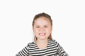 Angry girl looking at camera. Irritated girl with clenched teeth and open mouth is frowning face.. Posing a little girl wearing a striped shirt. Child can't handle her emotion. Dissatisfaction concept