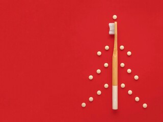 Bamboo toothbrush and eco toothpaste in tablets. Creative Christmas tree on the red background. Plastic free, zero waste.