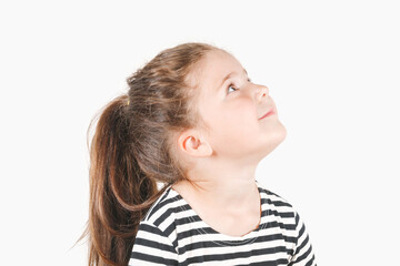 Side profile view of cute smiling girl looking up aside. Girl is waiting for something amazing, looking and listening with attention. Posing little girl wearing striped shirt.