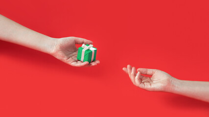 Funny creative concept of Christmas celebration. Modern art composition of X-mas gift presentation. Two human's hands with present on red background.