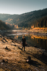 A hiking girl exploring a beautiful mountain lake with colorful autumn foilage and evening sunset light. Perfect warm fall day in the nature. Grane Dam, Granetalsperre, Harz Mountains