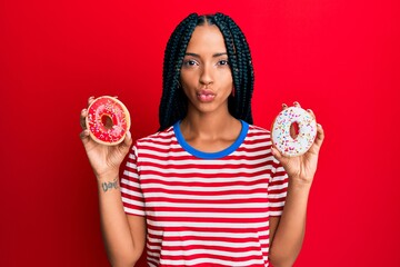 Beautiful hispanic woman holding tasty colorful doughnuts looking at the camera blowing a kiss being lovely and sexy. love expression.