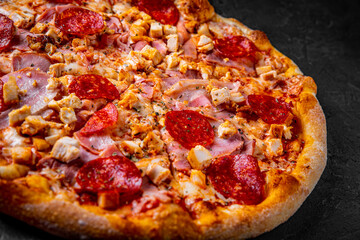 Pizza with Mozzarella cheese, salami, chicken meat, bacon, ham, Tomato sauce, pepper, spices. Italian pizza on Dark grey black slate background