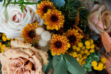 close up of seasonal autumn flower arrangement with yellow, orange, and cream roses, dahlias, and Craspedia blooms 