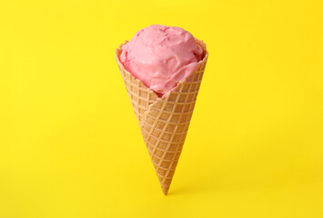 Delicious pink ice cream in waffle cone on yellow background