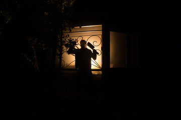 Fototapeta premium Silhouette of an unknown shadow figure on a door through a closed glass door. The silhouette of a human in front of a window at night.