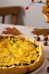 Quiche pie with mushrooms and cheese, autumn background with fallen maple and oak leaves, pine cones, rose hips and hazelnuts