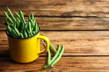 Fresh green beans in mug on wooden table, space for text