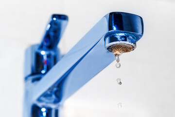 Water droplets drip from the chrome faucet in the kitchen sink or bathroom. The concept of the idea...
