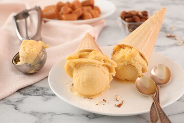 Plate with delicious yellow ice cream in wafer cones and spoons on white marble table, closeup