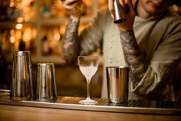 barman pouring drink from metal jigger into mixing cup on bar counter