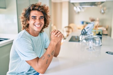 Young hispanic man smiling happy sitting on the table at home
