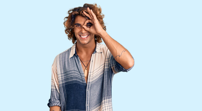 Young hispanic man wearing summer style doing ok gesture with hand smiling, eye looking through fingers with happy face.