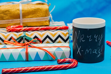 Merry x-mas inscription by chalk on a cup. Bunch of wrapped gift boxes on background. Christmas...