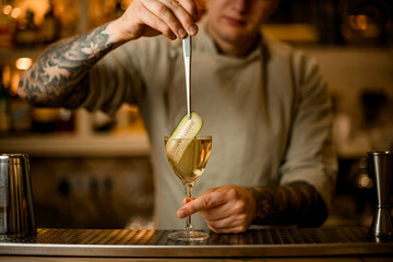 view of barman decorates cocktail glass with cucumber slice using tweezers
