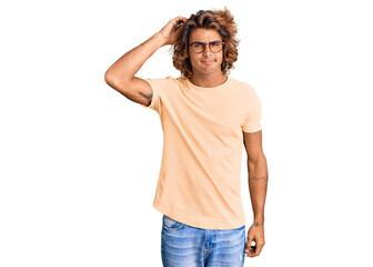 Young hispanic man wearing casual clothes and glasses confuse and wonder about question. uncertain...