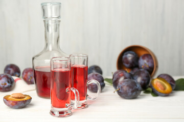 Delicious plum liquor and ripe fruits on white wooden table, space for text. Homemade strong alcoholic beverage