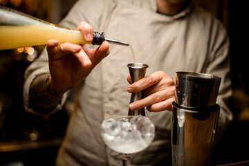 bartender carefully pours drink from bottle into metal jigger.