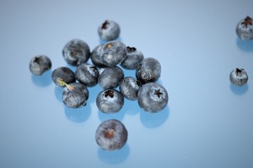 Fresh juicy Blueberries scattered and spilled over onto the surface of blue backlit background