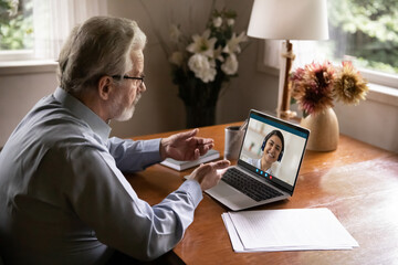 Side view focused elderly 60s businessman talking online with indian ethnicity female colleague,...