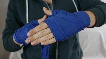 A woman in her arms, wrapped in boxing ribbons, prepares for a workout in the gym. Woman covers her hands with professional boxing bands