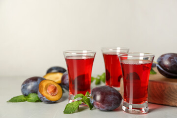 Delicious plum liquor, mint and ripe fruits on light table. Homemade strong alcoholic beverage