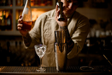 barman masterfully pours drink from metal jigger into shaker on bar counter