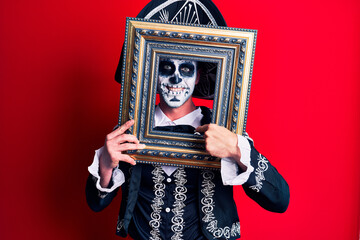 Fototapeta premium Young man wearing mexican day of the dead costume holding empty frame pointing finger to one self smiling happy and proud