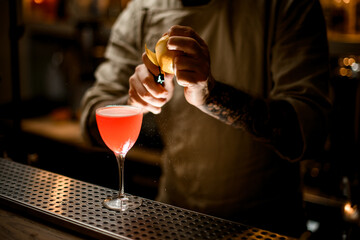 view on barman holds lemon and accurate cuts the peel off with knife
