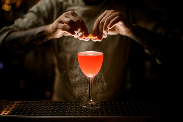 bartender holding lemon peel over glass with bright cocktail and sprinkles on it.