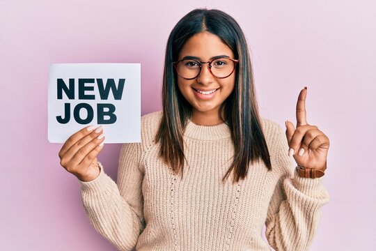 Young latin girl holding new job message on paper surprised with an idea or question pointing finger with happy face, number one