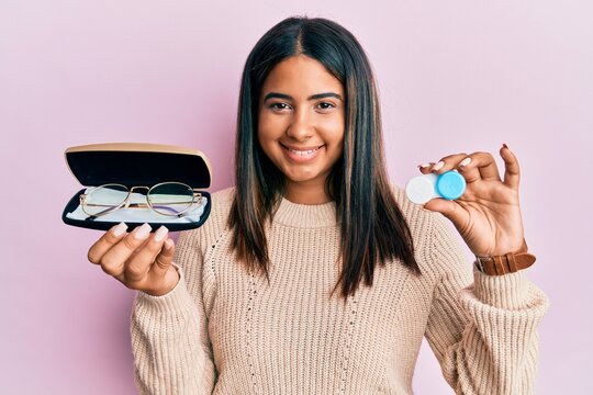 Young latin girl holding glasses and contact lenses smiling with a happy and cool smile on face. showing teeth.