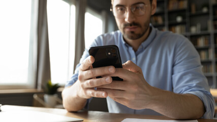Serious man manager using smartphone chat with client sit at desk in office, close up focus on...
