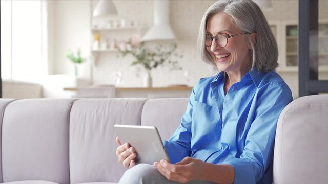 Happy old senior woman grandmother holding digital tablet video conference calling talking enjoying social distance party, virtual family online chat meeting with grandchildren on holiday at home.