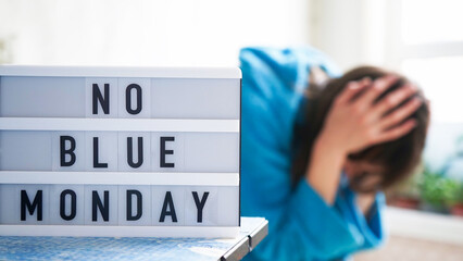 White board with text no blue monday on the table, in the background a woman in blue clothes depressed near the window,defocused.Blue monday day banner concept. Lettering.