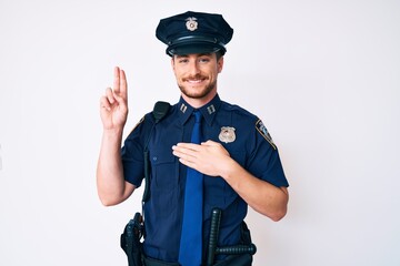 Young caucasian man wearing police uniform smiling swearing with hand on chest and fingers up, making a loyalty promise oath