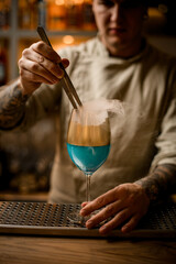 bartender holds piece of ice with tweezers and adds it to steaming wine glass