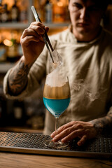 guy accurate holds piece of ice over steaming wine glass decorated with gold