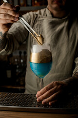 male barman gently holds golden piece of ice over steaming wine glass decorated with gold