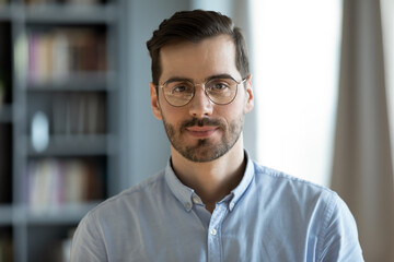 Head shot young attractive businessman in glasses standing in modern office pose for camera....