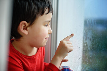 Little sick boy in pajamas looking through window. isolation at home. Stay at home quarantine...