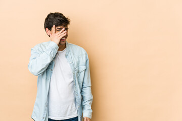Young cool man blink at the camera through fingers, embarrassed covering face.