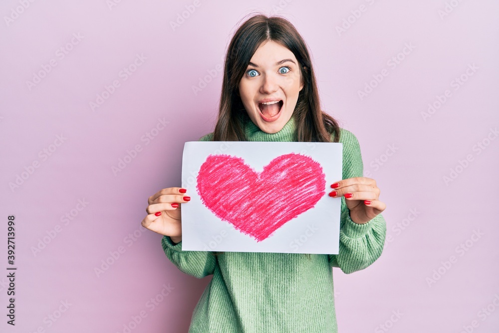 Sticker young beautiful caucasian girl holding heart draw celebrating crazy and amazed for success with open