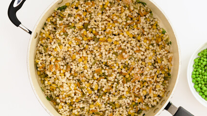 A savory blend of pearled couscous, orzo, baby garbanzo beans, red quinoa close up on frying pan on white background