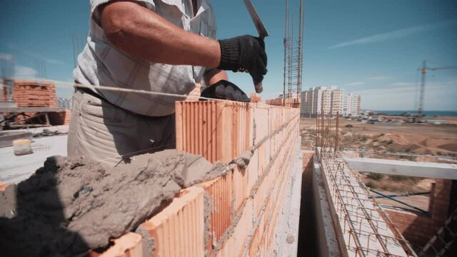 Professional worker rapidly gets red brick and place it on building wall