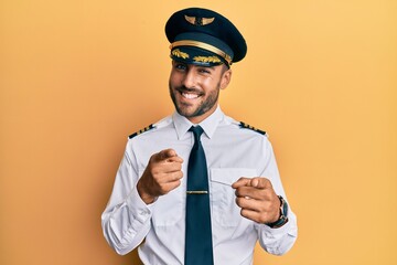 Handsome hispanic man wearing airplane pilot uniform pointing fingers to camera with happy and...