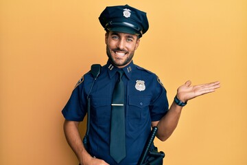 Handsome hispanic man wearing police uniform smiling cheerful presenting and pointing with palm of hand looking at the camera.