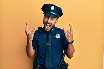 Handsome hispanic man wearing police uniform shouting with crazy expression doing rock symbol with hands up. music star. heavy music concept.