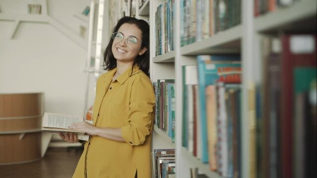people, knowledge, education and school concept - happy student girl or young woman with book in library