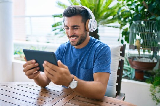 Young hispanic man smiling happy using tablet and headphones at the terrace.